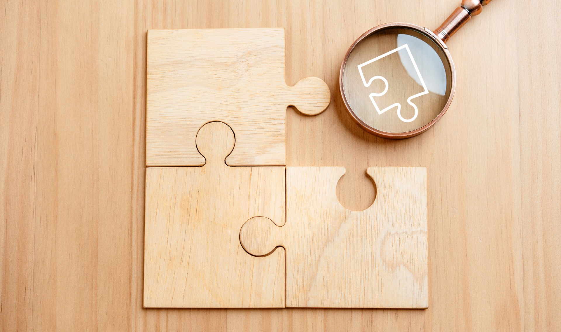 A puzzle is on a wooden table with a magnifying glass next to it.